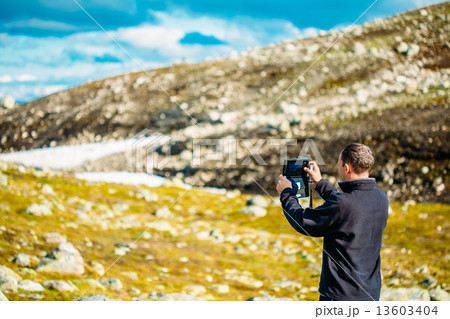 Young Man Taking Pictures Of Norwegian Mountain Landscape On Tab Young Man Taking Pictures Of Norwegian Mountain Landscape On Tab 13603404