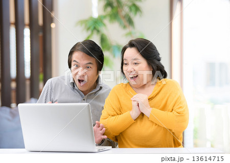 自宅のリビングでパソコンを操作している、カジュアルウェアー姿の中年夫婦 13614715