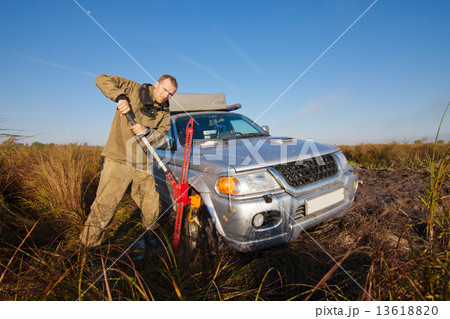 Man lifting car stucked in deep mud by hi jack Man lifting car stucked in deep mud by hi jack 13618820