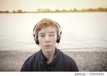 portrait of a teenage boy with headphones at a riverbank, toned 13648291