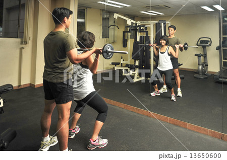 Asian woman is been guided by her male personal trainer during workout in indoor gym 13650600