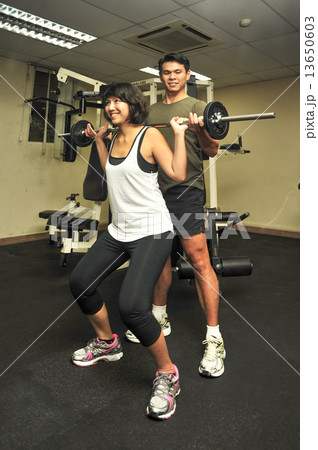 Asian woman is been guided by her male personal trainer during workout in indoor gym 13650603