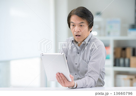 室内でタブレットを操作している、カジュアルウェアー姿の中年男性 13660796