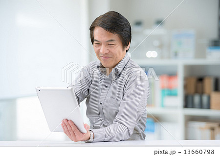 室内でタブレットを操作している、カジュアルウェアー姿の中年男性 室内でタブレットを操作している、カジュアルウェアー姿の中年男性 13660798