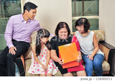 Asian mature woman opening her present infront of her family during the Christmas / birthday party Asian mature woman opening her present infront of her family during the Christmas / birthday party 13680051