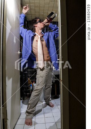 Drunk Man is standing in a toilet with a bottle of whiskey 13680439