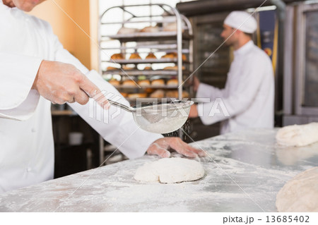 Baker sieving flour on the dough 13685402