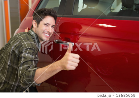 Smiling man hugging a red car while giving thumbs up 13685659