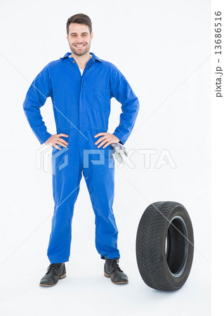 Smiling mechanic with hands on hips standing by tire Smiling mechanic with hands on hips standing by tire 13686516