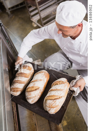 Baker taking tray of fresh bread out of oven Baker taking tray of fresh bread out of oven 13686902