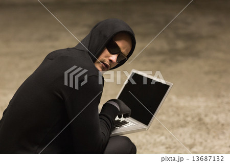 Hacker in hooded jumper using laptop 13687132