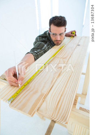 Worker using measure tape to mark on wooden plank 13687304
