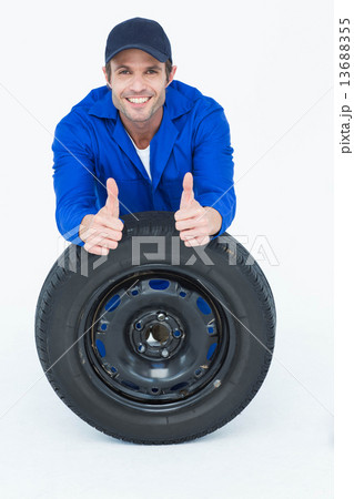 Mechanic leaning on tire while gesturing thumbs up 13688355