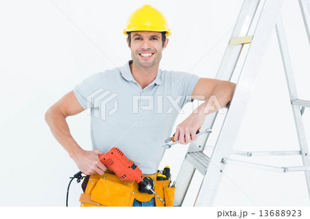 Technician holding drill machine while leaning on step ladder Technician holding drill machine while leaning on step ladder 13688923