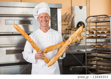Smiling baker holding three baguettes Smiling baker holding three baguettes 13689303