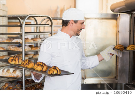 Smiling baker holding trays of croissants Smiling baker holding trays of croissants 13690410