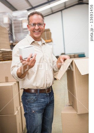 Smiling warehouse worker holding small box 13691456