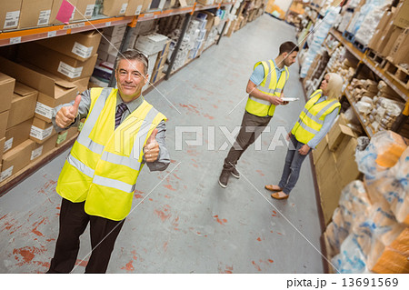 Warehouse manager smiling at camera showing thumbs up Warehouse manager smiling at camera showing thumbs up 13691569