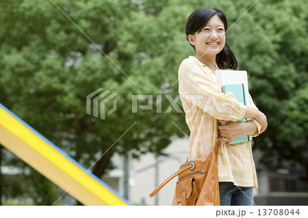 笑顔で本を抱えて立つ若い女性の写真素材