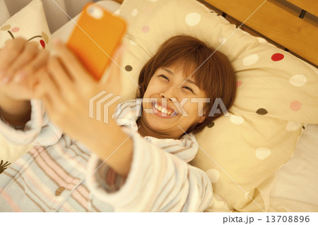ベッドに寝転んでスマートフォンを操作する女性 ベッドに寝転んでスマートフォンを操作する女性 13708896