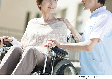 車いすに乗った中高年女性に寄り添う介護士 13708965
