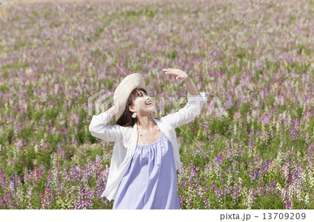 花畑で麦わら帽子を押さえて手をかざす笑顔の女性 花畑で麦わら帽子を押さえて手をかざす笑顔の女性 13709209