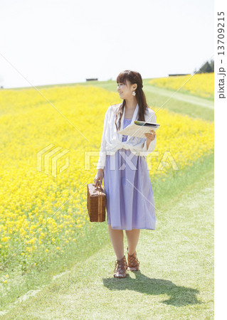 地図を持って菜の花畑を歩く笑顔の女性 13709215