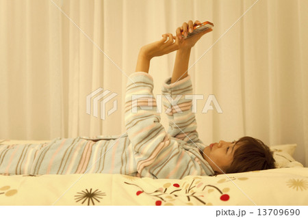 ベッドに寝転んでスマートフォンを操作する女性 13709690