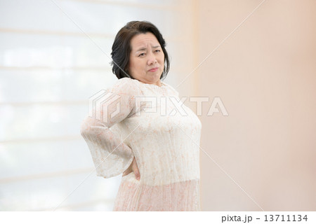 室内に立っている、腰痛、肩こりに悩んでいるカジュアルウェアー姿の中年女性 13711134