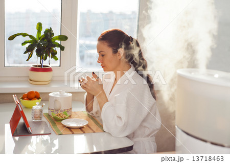Woman drinking tea reading tablet at humidifier 13718463