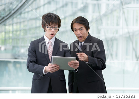 近代的な建物の中にタブレットを持って立っているスーツ姿の2人の男性 13725233