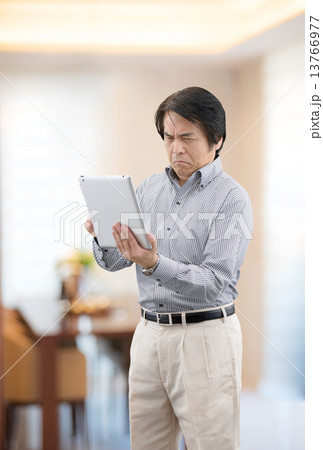 自宅リビングでタブレットを操作しているカジュアルウェアー姿の中年男性 13766977