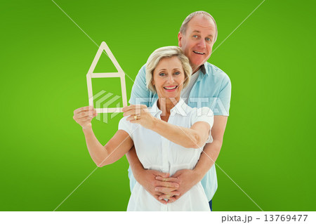 Composite image of happy older couple holding house shape 13769477