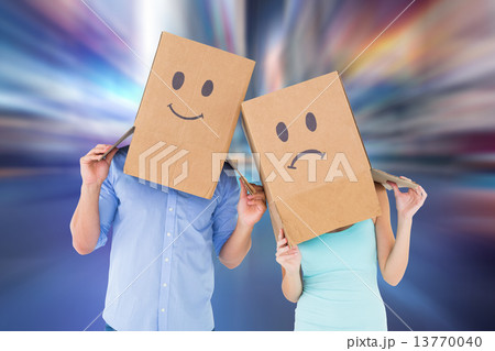 Composite image of couple wearing sad face boxes on their heads 13770040
