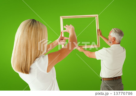Composite image of couple hanging a frame together 13770786