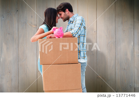 Composite image of happy young couple with moving boxes and pigg Composite image of happy young couple with moving boxes and pigg 13771446