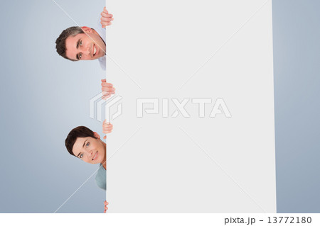Composite image of woman and man hiding behind a blank panel 13772180