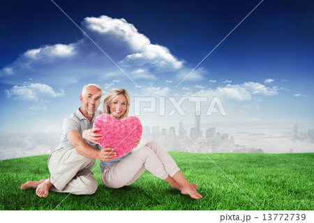 Composite image of happy couple sitting and holding heart pillow 13772739