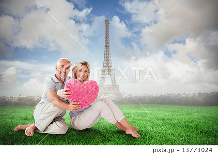 Composite image of happy couple sitting and holding heart pillow 13773024