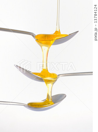 Honey dripping over three silver teaspoonful 13784124