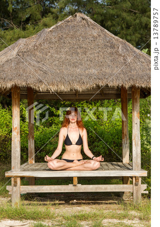 Woman doing yoga meditation in tropical gazebo 13789757