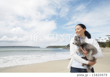 犬を抱いて砂浜に立つ女性 13820979