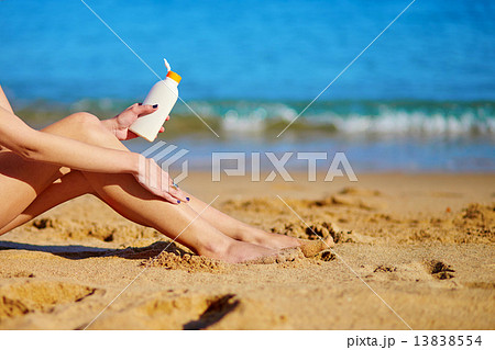 Beautiful woman applying sunscreen on her legs 13838554