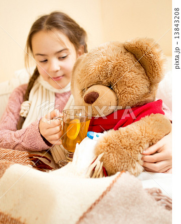 sick girl lying in bed and giving tea to teddy bear 13843208
