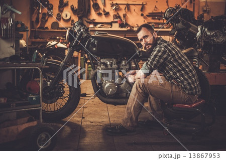 Mechanic building vintage style cafe-racer motorcycle  in custom garage 13867953
