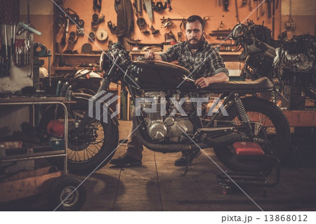 Mechanic building vintage style cafe-racer motorcycle  in custom garage 13868012