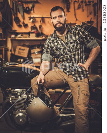 Rider and his vintage style cafe-racer motorcycle in customs garage 13868028