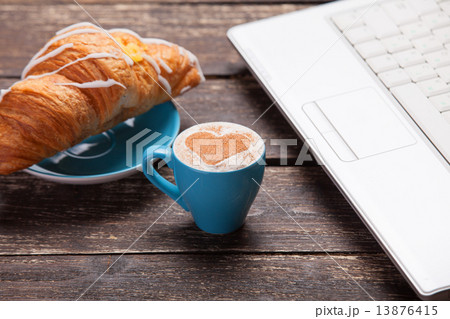 Croissant and cup of coffee with laptop on wooden table. 13876415