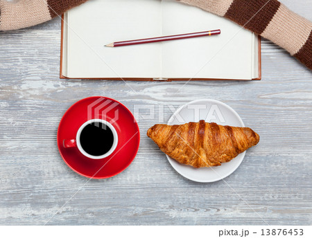 Cup, croissant and book with scarf on wooden table. 13876453