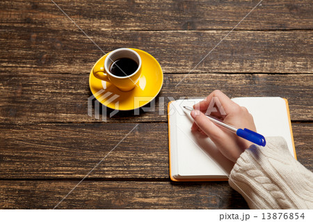 Female hand writing something in notebook near cup of coffee. Female hand writing something in notebook near cup of coffee. 13876854